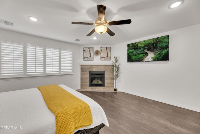 bedroom with a tiled fireplace, wood finished floors, visible vents, and baseboards