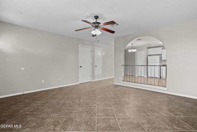 unfurnished room with arched walkways, ceiling fan with notable chandelier, and baseboards