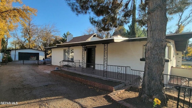 view of front facade featuring an outbuilding, a porch, a chimney, and stucco siding