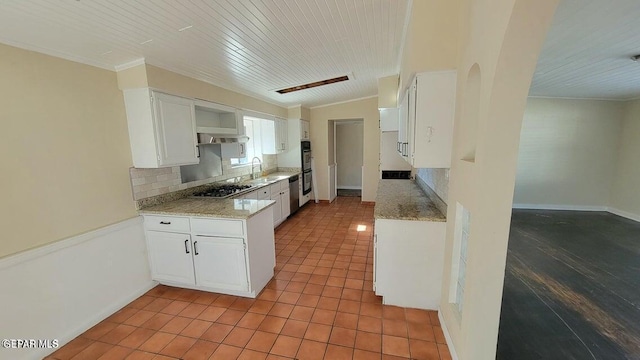 kitchen with ornamental molding, decorative backsplash, a sink, white cabinets, and tile patterned floors