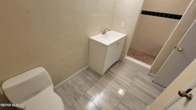 bathroom featuring vanity, toilet, baseboards, and tiled shower