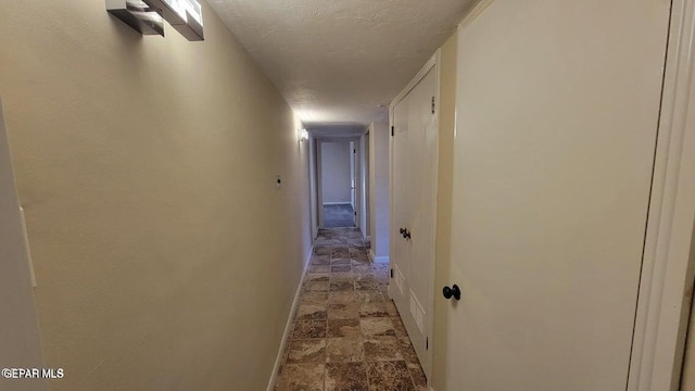 hall featuring stone finish floor, a textured ceiling, and baseboards