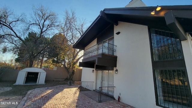 view of property exterior with an outbuilding, a balcony, fence, stucco siding, and a patio area