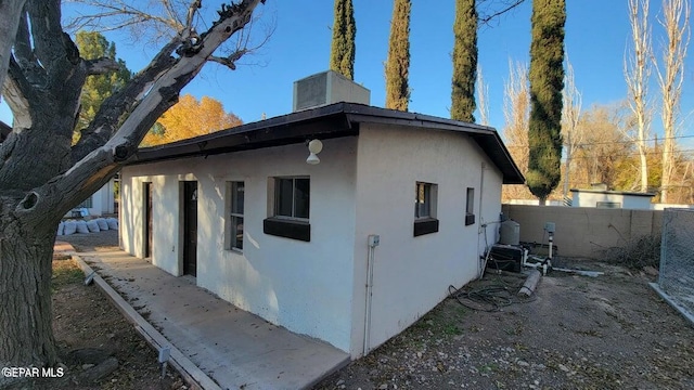 view of side of home featuring stucco siding, central AC, and fence