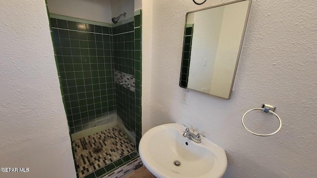 bathroom featuring a stall shower, a textured wall, and a sink