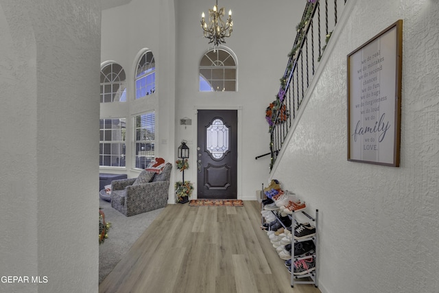 entryway with wood finished floors, an inviting chandelier, a high ceiling, stairs, and a textured wall