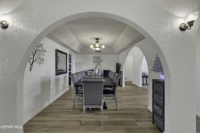 dining area with a tray ceiling, wood finished floors, baseboards, a chandelier, and a textured wall