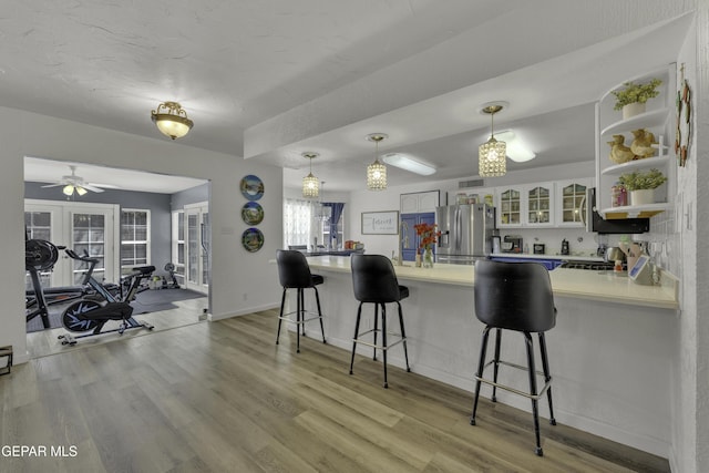 kitchen featuring a breakfast bar, a peninsula, glass insert cabinets, and stainless steel fridge with ice dispenser