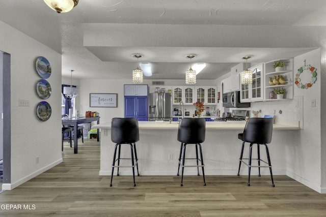 kitchen featuring a kitchen bar, appliances with stainless steel finishes, a peninsula, and light wood finished floors