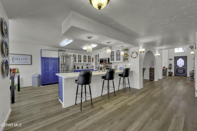 kitchen featuring a peninsula, arched walkways, stainless steel appliances, a kitchen bar, and blue cabinets