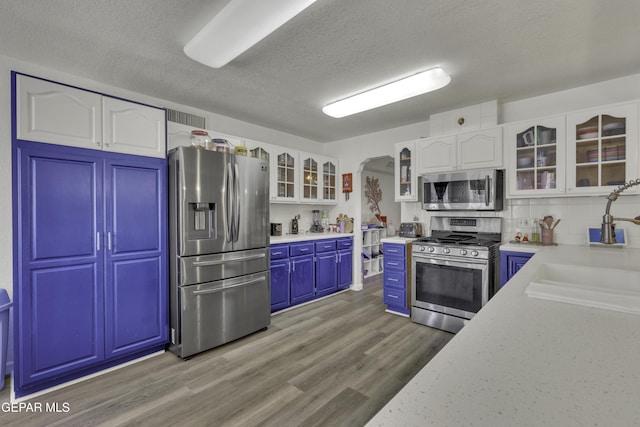 kitchen with a sink, arched walkways, white cabinetry, and stainless steel appliances