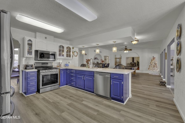 kitchen with appliances with stainless steel finishes, a peninsula, white cabinets, blue cabinets, and a sink