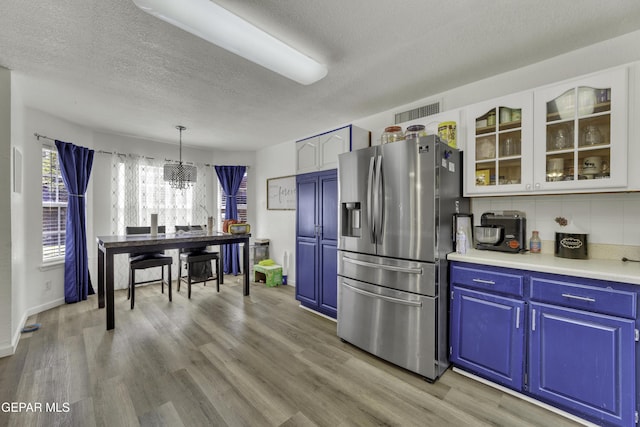 kitchen with blue cabinetry, glass insert cabinets, stainless steel fridge with ice dispenser, an inviting chandelier, and light wood-style floors