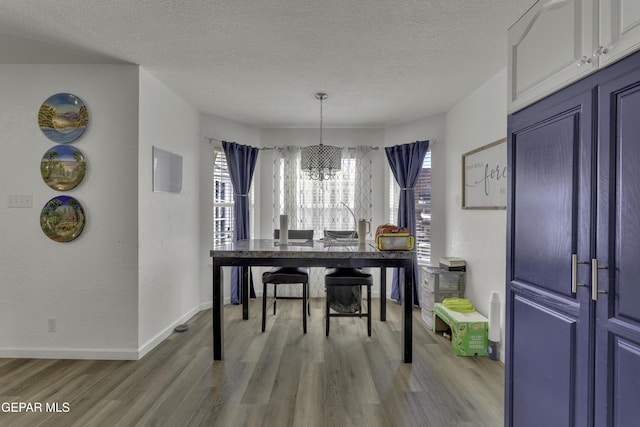 dining space with a notable chandelier, light wood-style flooring, a textured ceiling, and a healthy amount of sunlight