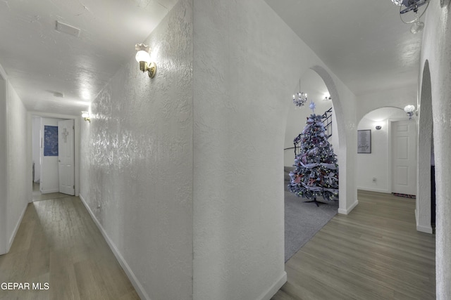 hallway featuring arched walkways, baseboards, a textured wall, and wood finished floors