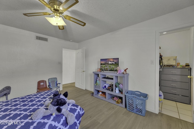 bedroom with visible vents, a textured ceiling, ceiling fan, and wood finished floors