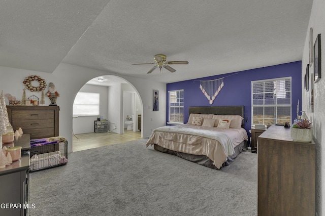 bedroom featuring arched walkways, ceiling fan, a textured ceiling, and carpet