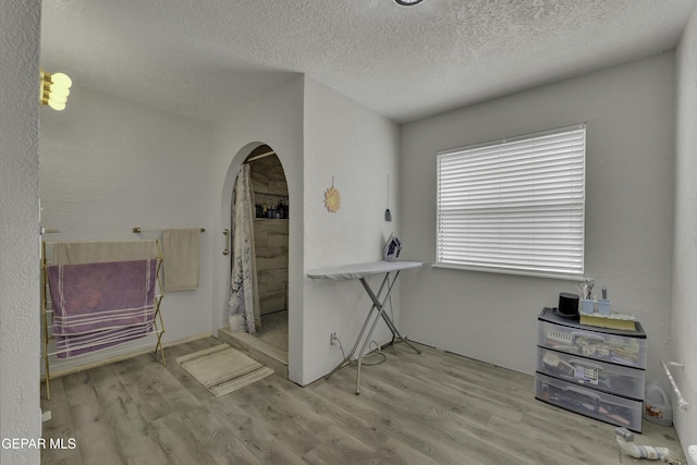 misc room featuring arched walkways, a textured ceiling, and wood finished floors