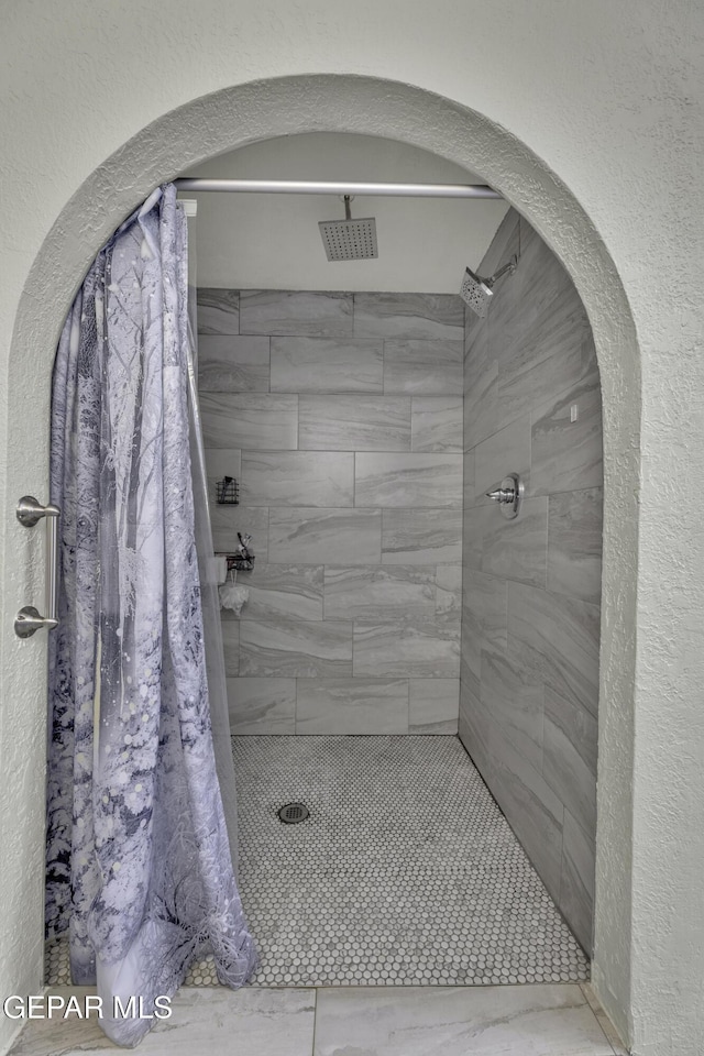 full bath with a textured wall and a tile shower