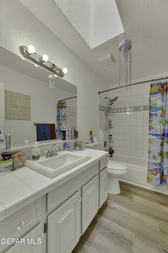 bathroom with vanity, wood finished floors, shower / bath combo, a textured ceiling, and toilet