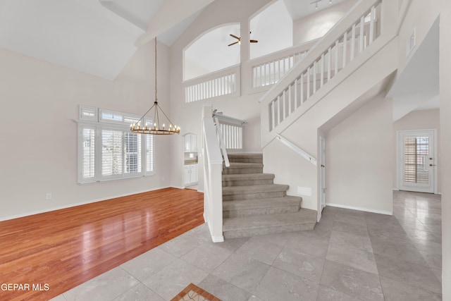 stairs with wood finished floors, visible vents, baseboards, a towering ceiling, and ceiling fan with notable chandelier