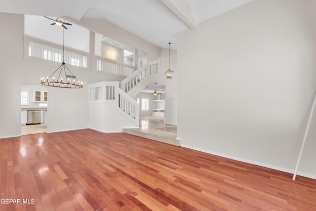 unfurnished living room with beamed ceiling, a healthy amount of sunlight, wood finished floors, and ceiling fan with notable chandelier