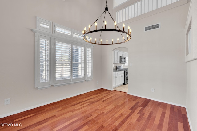 unfurnished dining area featuring an inviting chandelier, baseboards, visible vents, and light wood-type flooring