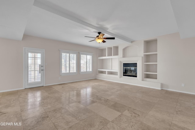 unfurnished living room featuring a glass covered fireplace, baseboards, built in shelves, and ceiling fan