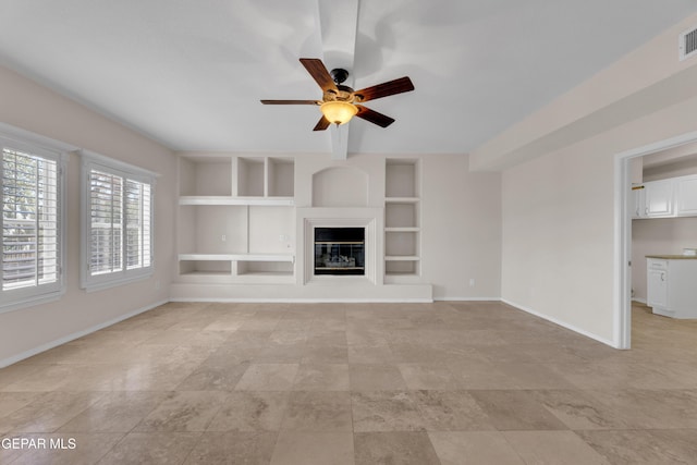 unfurnished living room with built in shelves, visible vents, baseboards, ceiling fan, and a glass covered fireplace