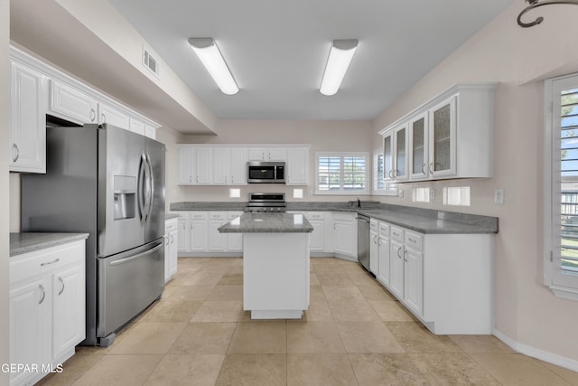 kitchen with a center island, glass insert cabinets, light tile patterned floors, white cabinets, and stainless steel appliances