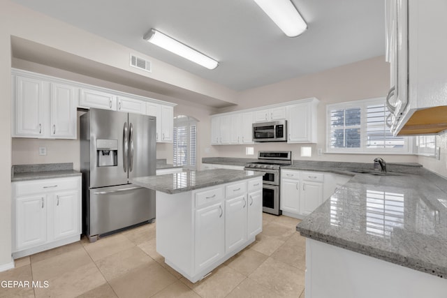 kitchen with light stone countertops, a kitchen island, a sink, appliances with stainless steel finishes, and white cabinetry