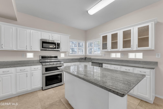 kitchen featuring a center island, white cabinetry, appliances with stainless steel finishes, glass insert cabinets, and light stone countertops