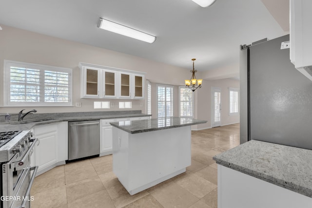 kitchen with glass insert cabinets, appliances with stainless steel finishes, a notable chandelier, white cabinets, and a sink