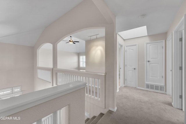 hallway with visible vents, track lighting, carpet, lofted ceiling with skylight, and arched walkways