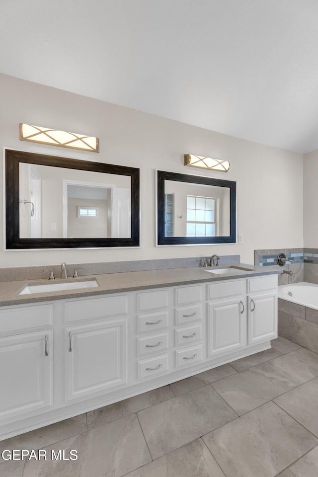 bathroom with double vanity, a relaxing tiled tub, marble finish floor, and a sink