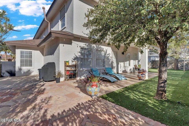 rear view of property featuring stucco siding, a lawn, and a patio area