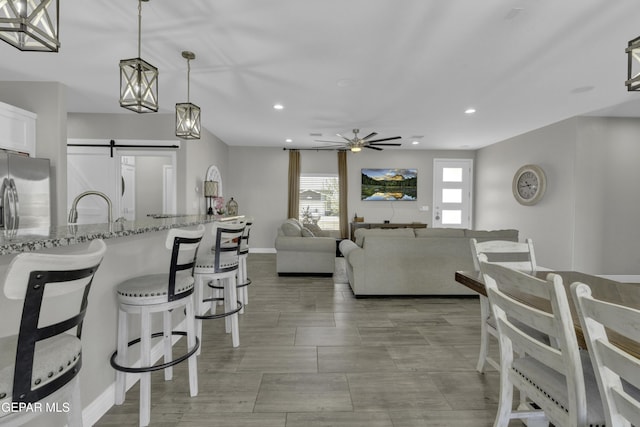 kitchen featuring light stone counters, a sink, white cabinetry, a kitchen breakfast bar, and stainless steel fridge