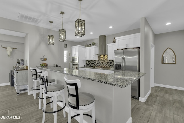 kitchen featuring visible vents, wall chimney range hood, a kitchen bar, decorative backsplash, and stainless steel appliances