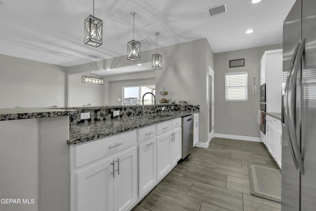 kitchen featuring visible vents, dark stone counters, a sink, stainless steel appliances, and white cabinets