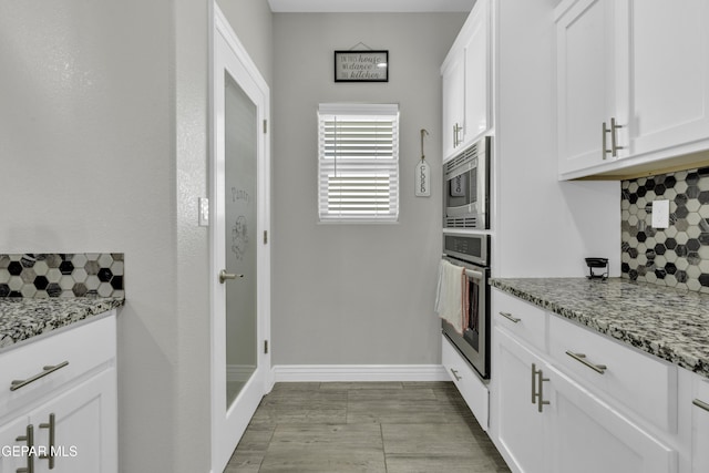 kitchen with white cabinetry, stainless steel appliances, baseboards, decorative backsplash, and light stone countertops