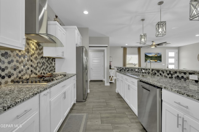 kitchen with a sink, stainless steel appliances, white cabinetry, and wall chimney range hood