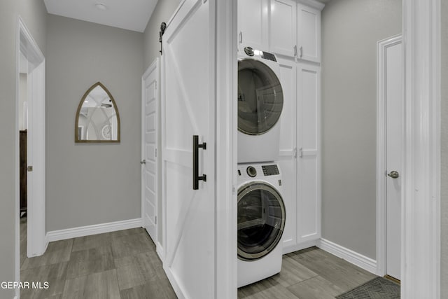 clothes washing area featuring a barn door, cabinet space, stacked washer / drying machine, and baseboards