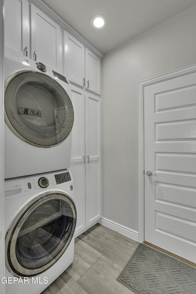 laundry room featuring baseboards, recessed lighting, cabinet space, light wood-style floors, and stacked washer / drying machine