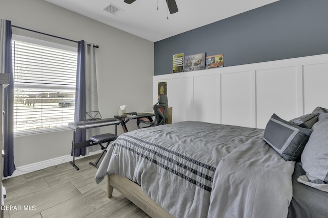 bedroom with a decorative wall, a ceiling fan, visible vents, and wainscoting