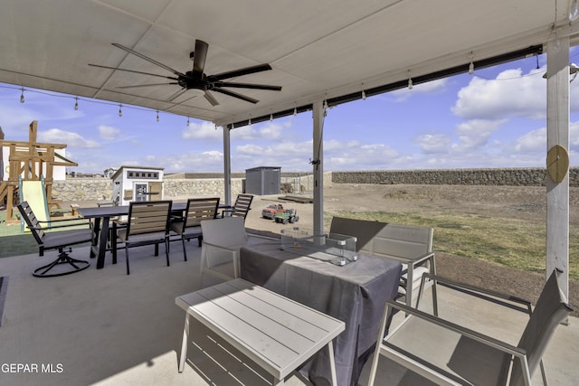 view of patio featuring outdoor dining space, an outbuilding, a playground, and a ceiling fan