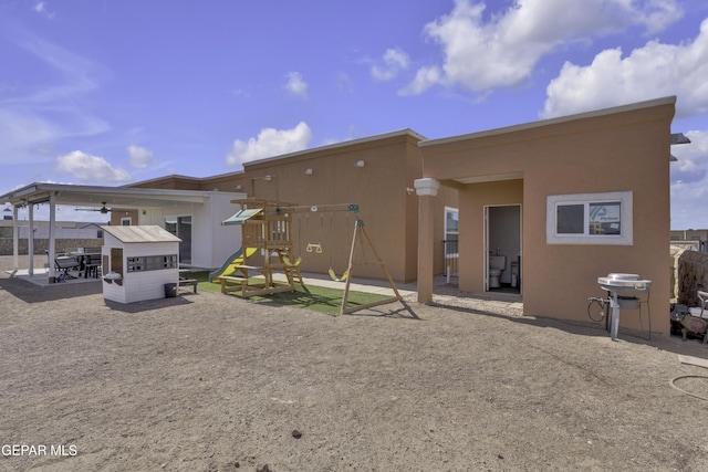 back of house with stucco siding and a playground