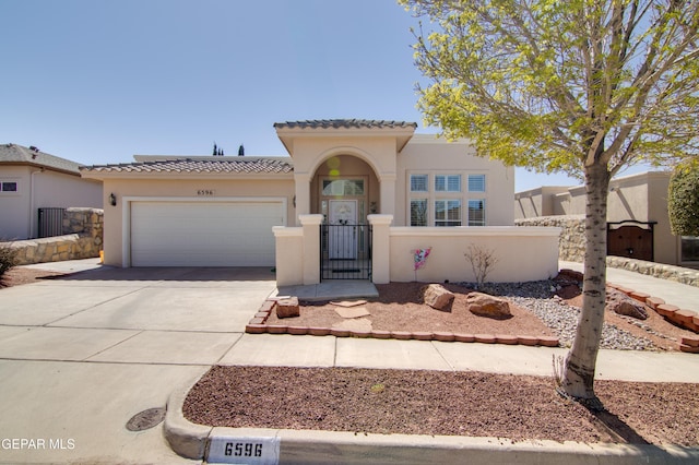 mediterranean / spanish home featuring a fenced front yard, a tiled roof, stucco siding, a garage, and driveway