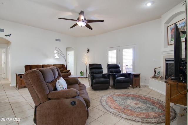 living room with visible vents, ceiling fan, light tile patterned floors, a tile fireplace, and arched walkways