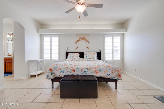 bedroom featuring light tile patterned floors, arched walkways, a ceiling fan, and baseboards