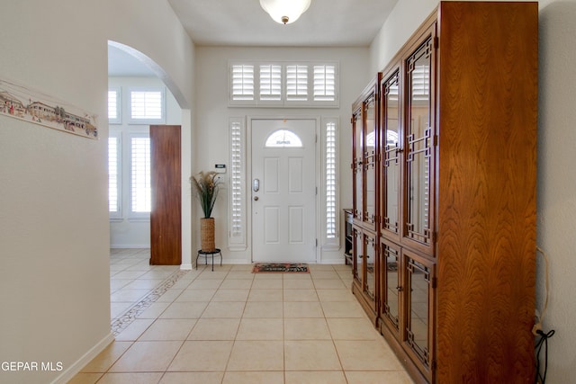 foyer entrance featuring arched walkways, baseboards, and light tile patterned flooring